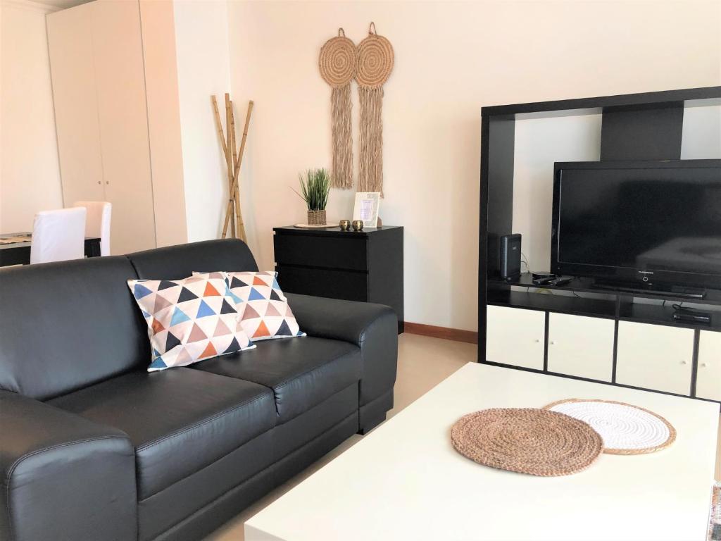 ein Wohnzimmer mit einem schwarzen Ledersofa und einem Flachbild-TV in der Unterkunft Apartamento Mar com Parking in Nazaré