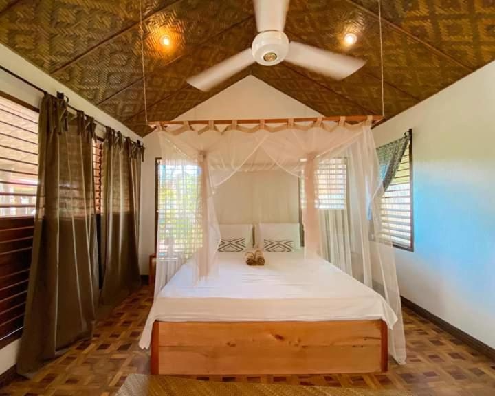 a bedroom with a canopy bed with a ceiling fan at Herbs Guest House and Restaurant near the Sea in Moalboal