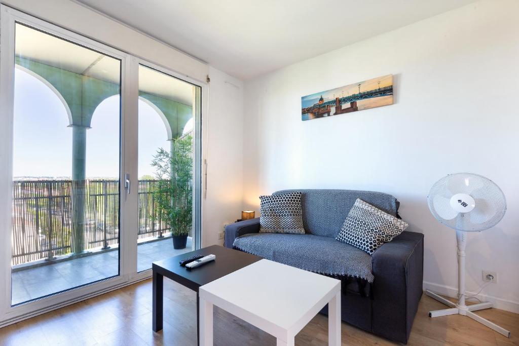 uma sala de estar com um sofá, uma mesa e uma janela em T2 climatisé avec piscine au pied du tram arènes romaines em Toulouse