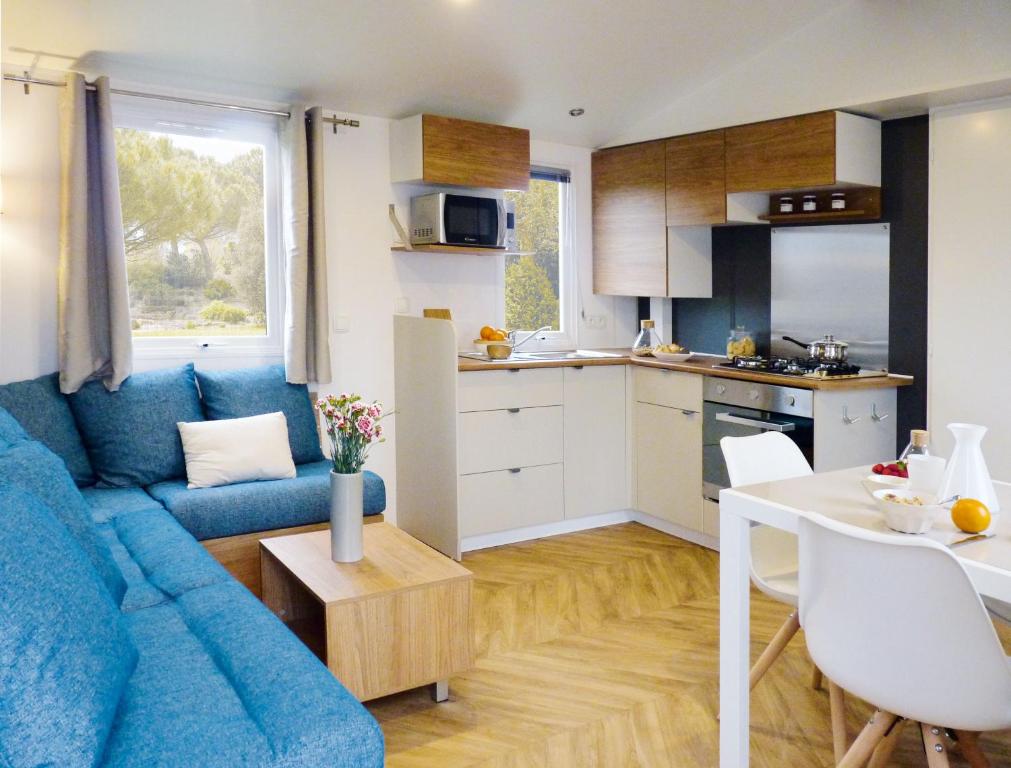 un salon avec un canapé bleu et une cuisine dans l'établissement Charmant mobile-home 6 personnes - Camping 4 étoiles, à Saint-Jean-de-Monts