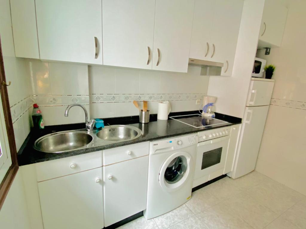 a white kitchen with a sink and a washing machine at A boa vista in Melide