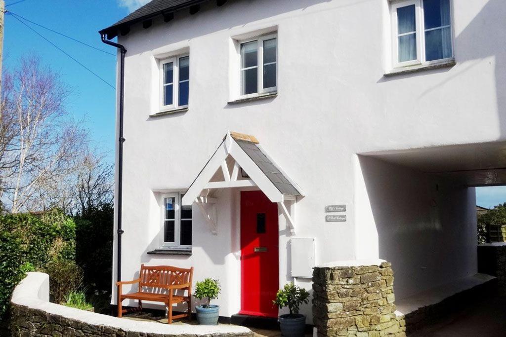 ein weißes Haus mit einer roten Tür und einer Bank in der Unterkunft Ollie's Cottage in Dittisham