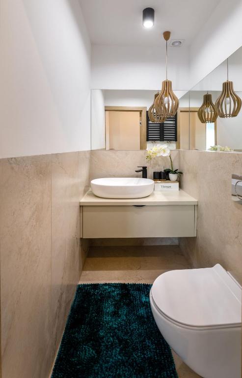Compact bathroom with white vessel sink, teal rug, hanging wooden pendant lights, clean neutral tiles