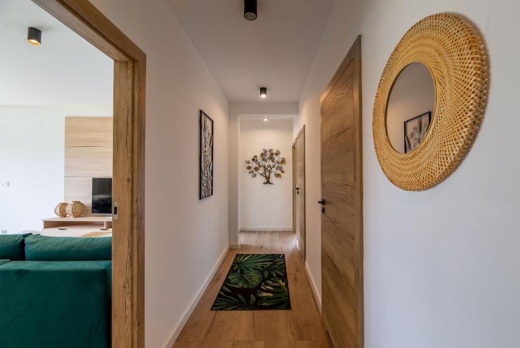 Bright hallway with rattan mirror, wooden doors, leafy rug, tree wall art, glimpse of living room