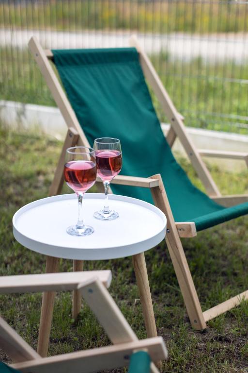 Two rosé glasses on small white table beside green canvas deck chairs on grass