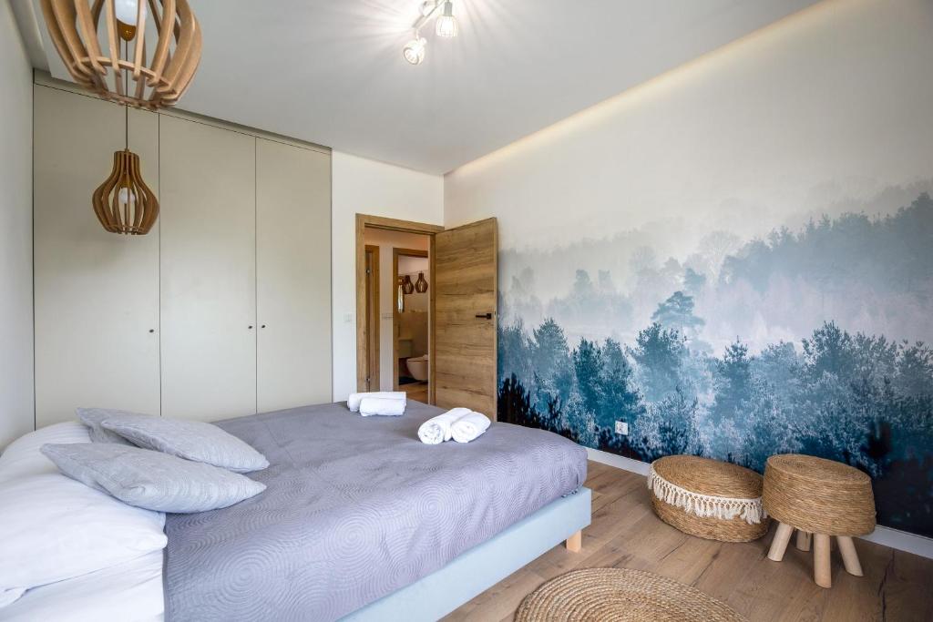 Calm bedroom with grey bedspread, built-in wardrobes, misty forest mural and woven poufs.