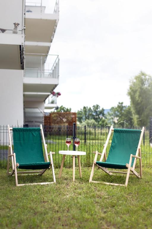 Two green deck chairs and small table with wine glasses on grassy lawn outside apartment.