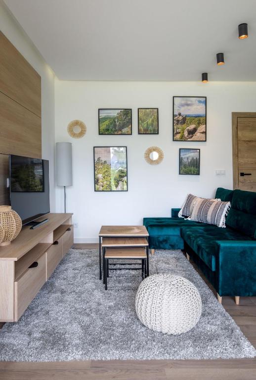 Cozy living room with deep teal sectional, wall art, TV unit, knitted pouf on rug.