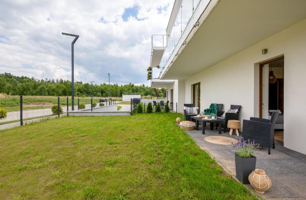 Ground-level apartment patio with wicker seating, small tables, and expansive grassy lawn.