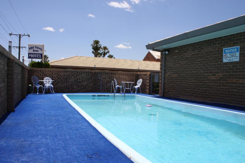 a swimming pool with chairs and a brick wall at Mid Town Inn Narrabri in Narrabri
