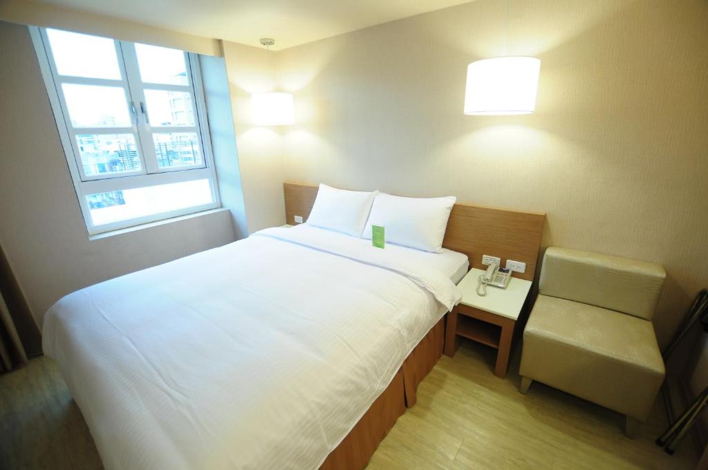 a bedroom with a large white bed and a chair at Kindness Hotel - Tainan Chihkan Tower in Tainan