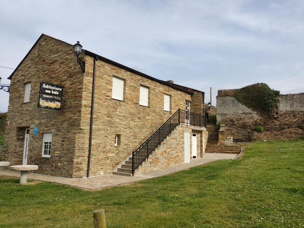 a brick building with a staircase next to a grass field at OS MUIÑOS in Ribadeo