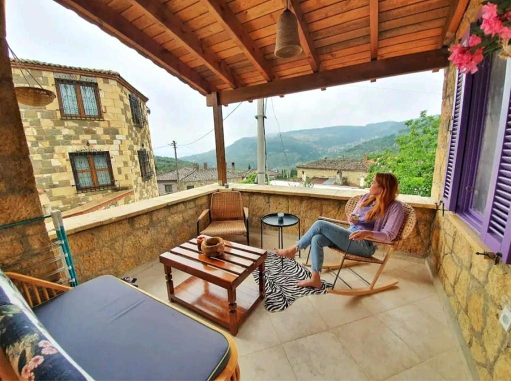 une femme assise sur le balcon d'une maison dans l'établissement Yerden Isıtma ve Şömineli Salvia - Sakin ve Bohem, à Ayvacık