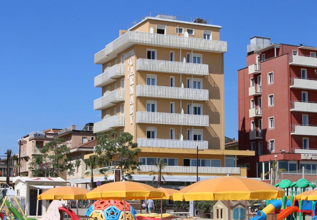 里米尼的住宿－卡納比酒店，海滩前高大的建筑,有遮阳伞