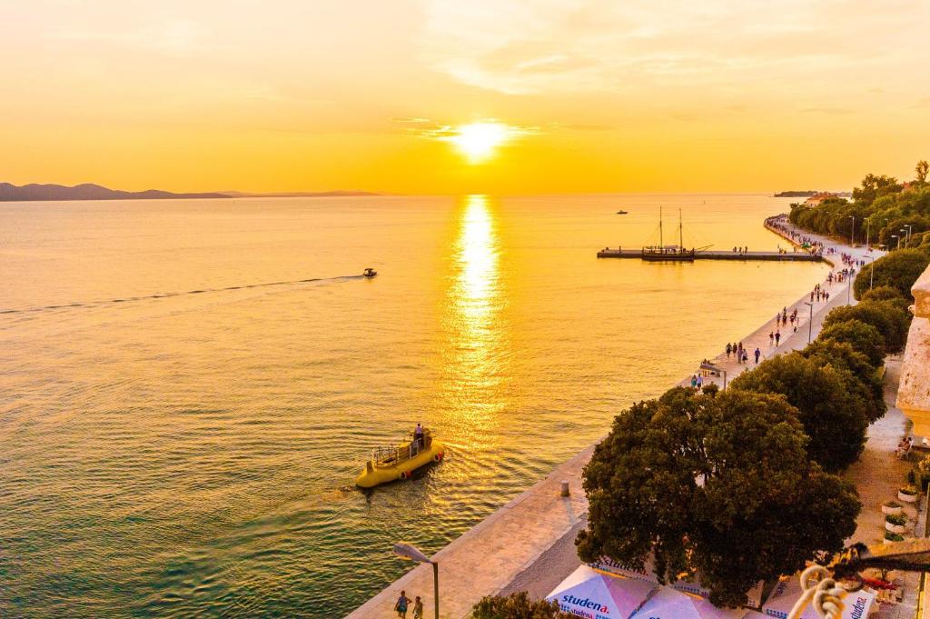 un barco en el agua con la puesta de sol en el fondo en Bristol lux 3BR apartment with view, en Zadar