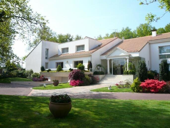 una gran casa blanca con un patio con una planta en Les Jardins de la Muse, piscine couverte, spa et fitness en Basse-Goulaine