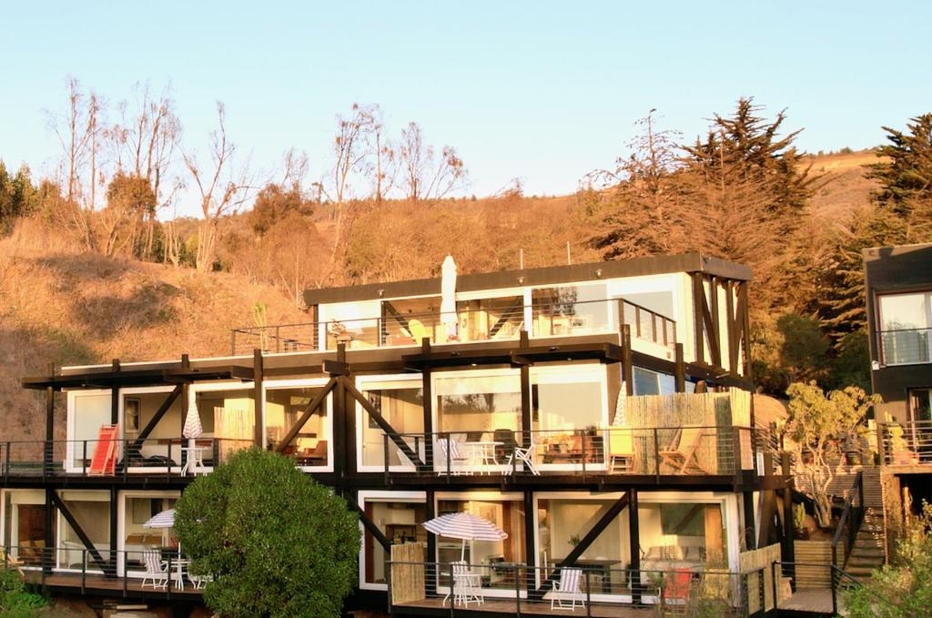 ein großes Haus mit einem Balkon mit Tischen und Stühlen in der Unterkunft Lofts Casa El Pangue Zapallar in Zapallar