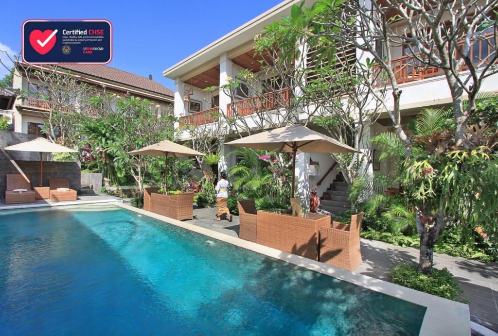 una piscina di fronte a un edificio con sedie e ombrelloni di Tebesaya Cottage by Pramana Villas ad Ubud