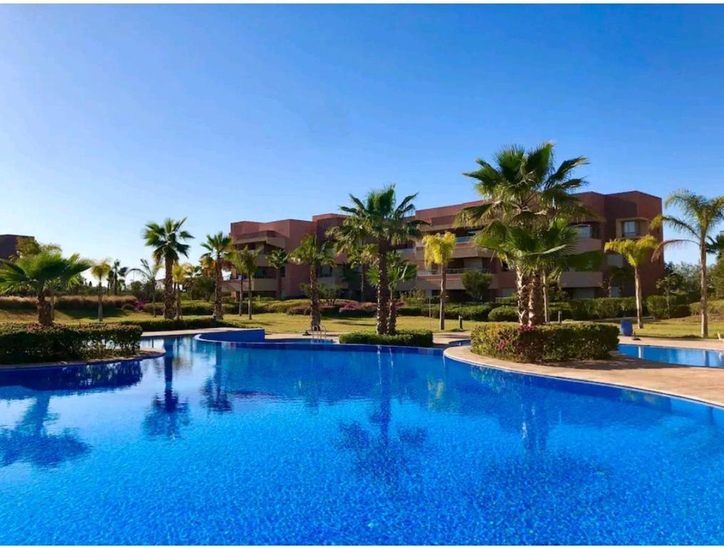 a large swimming pool with palm trees in front of a building at Marrakech golf city prestigia in Marrakech