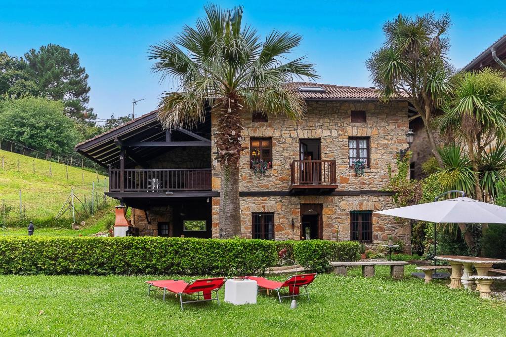 una casa con una palmera, sillas y una sombrilla en Caserio Urikosolo, en Bilbao