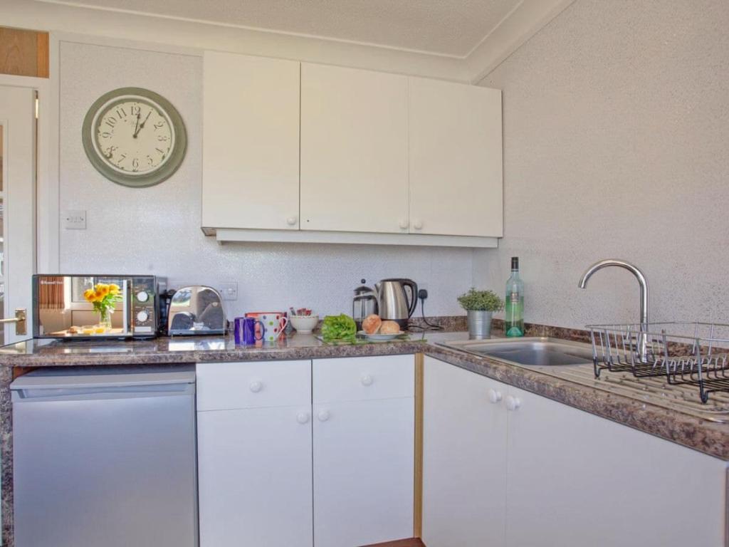 a kitchen with white cabinets and a clock on the wall at Dawlish Warren Holidays in Dawlish