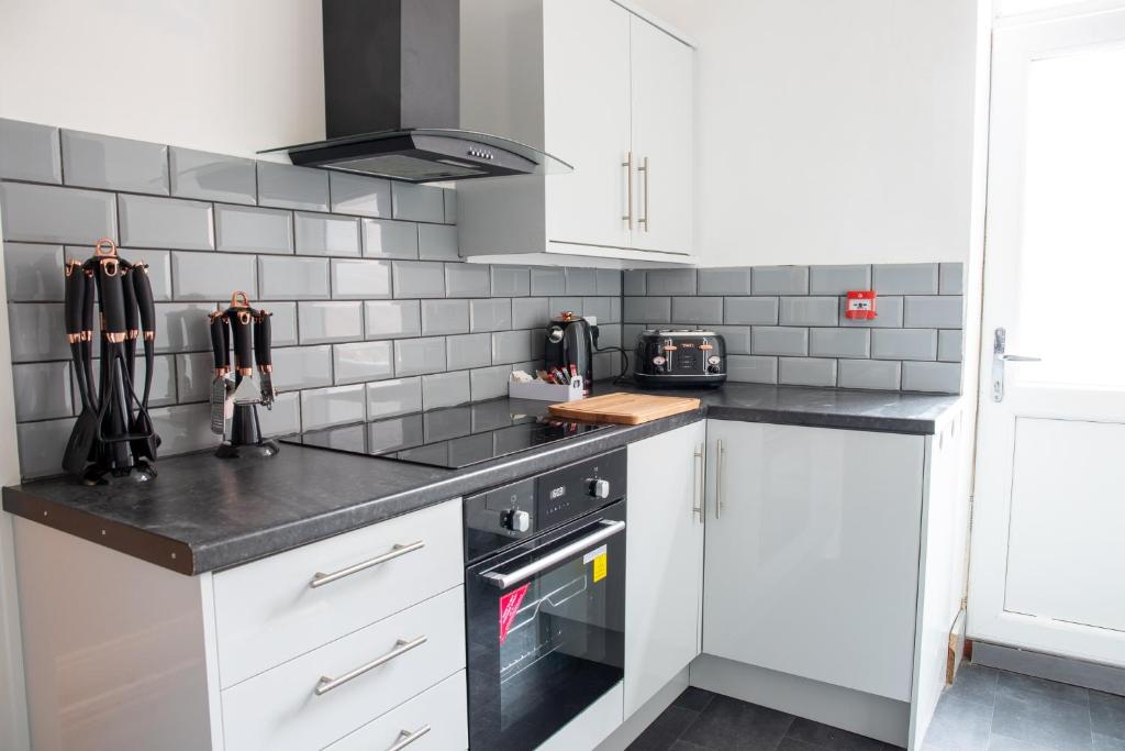 a kitchen with white cabinets and black counter tops at Withnell Stays - Apartment One - Ground Floor - Retro Gaming Machine in Blackpool