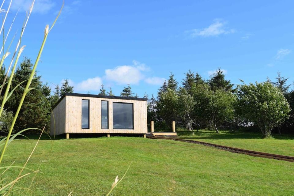 a small house on a grassy field with trees at Modern cabin with stunning views & private hot tub in Breakish