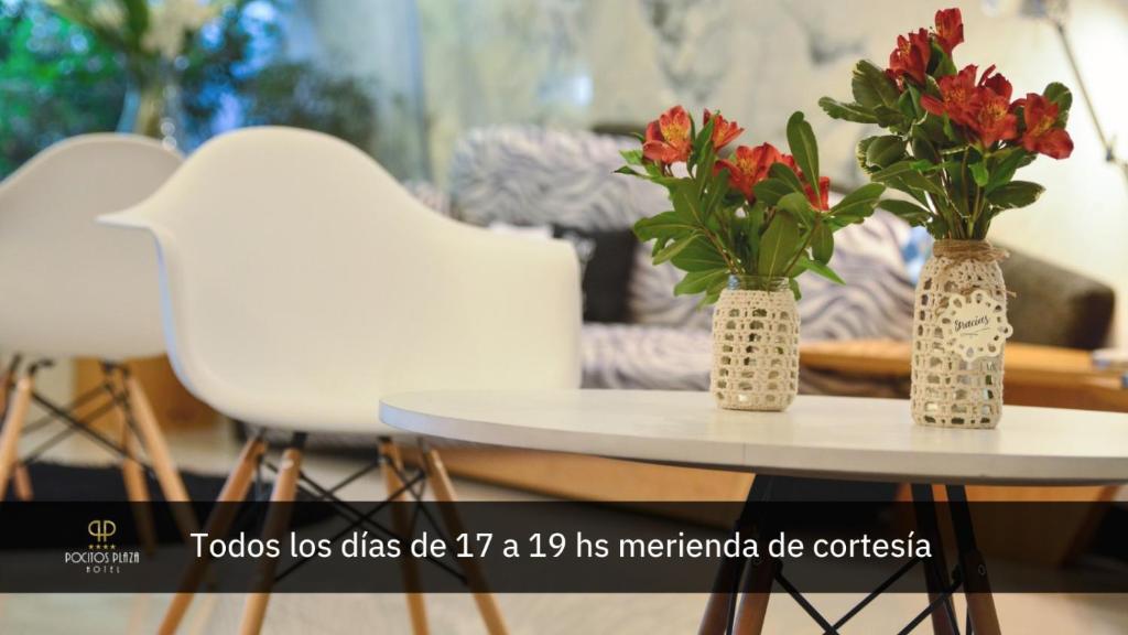 duas cadeiras brancas e dois vasos com flores sobre uma mesa em Pocitos Plaza Hotel em Montevidéu