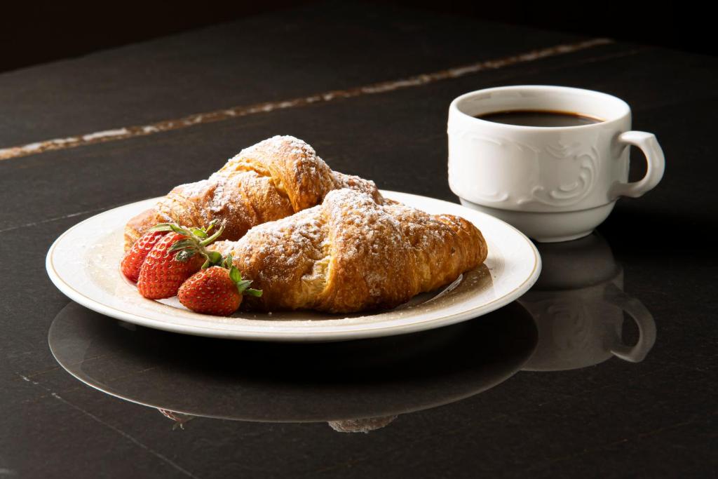 a plate with two croissants and strawberries next to a cup of coffee at Hotel Villa Romeo in Catania