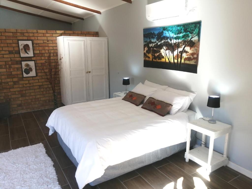 1 dormitorio con cama blanca y pared de ladrillo en Thatchers Guest Rooms en Welkom