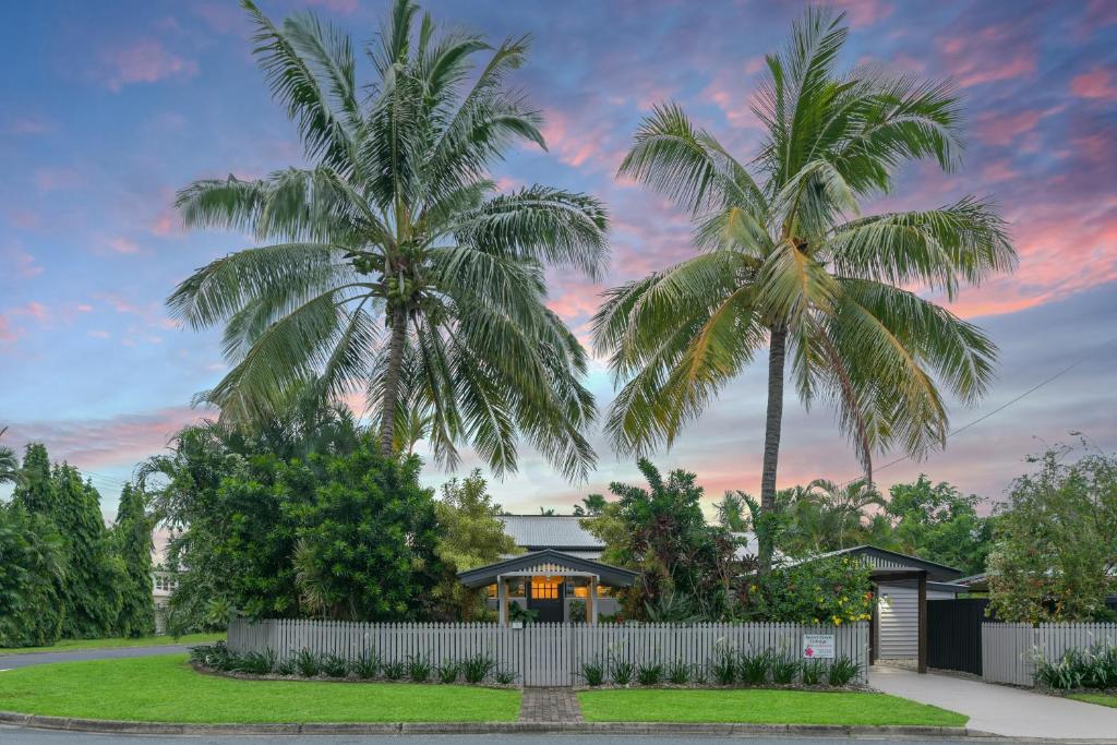 two palm trees in front of a house with a fence at Sweet Creek Cottage, Palm Cove, 200m to Beach, Heated Pool, Pets in Palm Cove