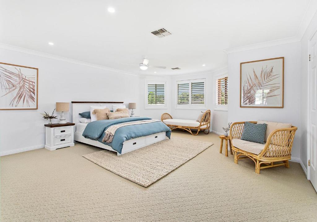 a white bedroom with a bed and a chair at Beach Haven in Shoalhaven Heads