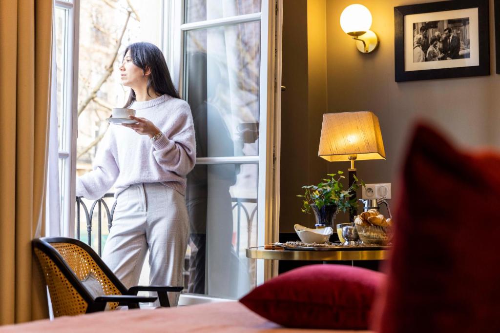 Una donna in piedi fuori da una finestra con una tazza di caffè di Welcome Hotel a Parigi