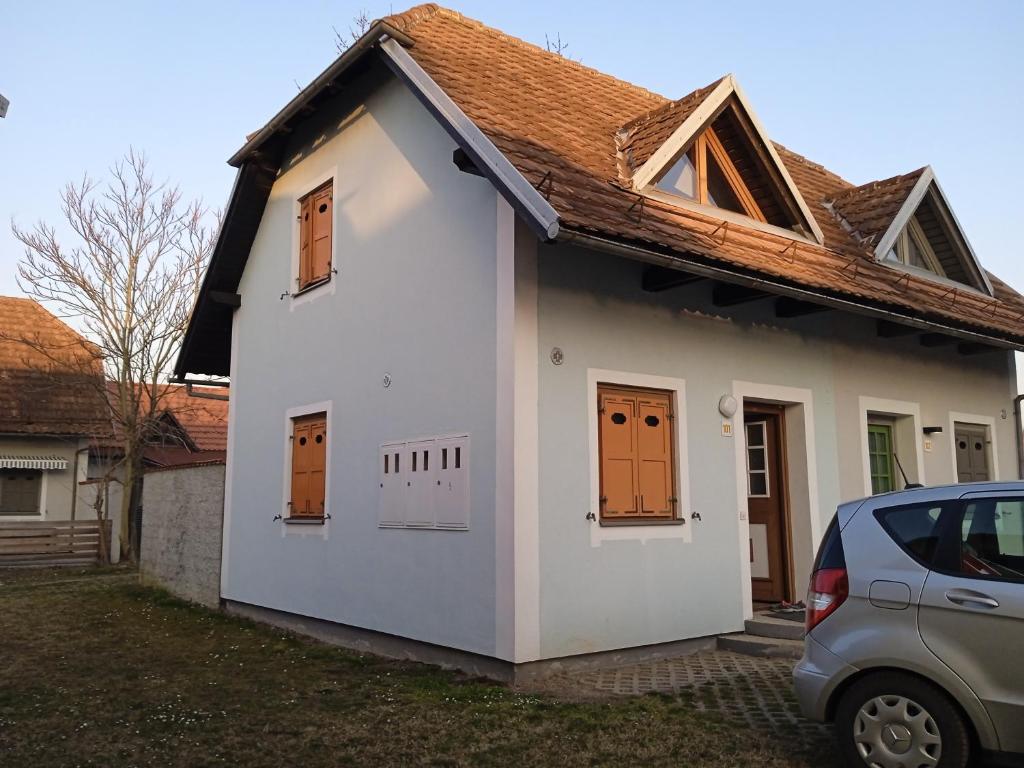 une petite maison blanche avec des portes orange et une voiture dans l'établissement Čebelica, apartma 101, Terme Čatež, à Brežice