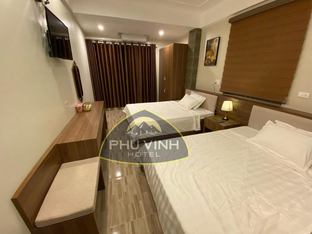 クアローにあるPhú Vinh Hotelのベッド2台とデスクが備わるホテルルームです。