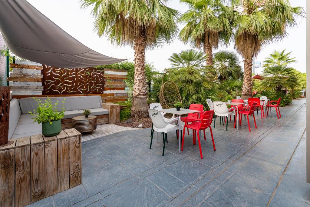 un patio con sillas rojas, mesas y palmeras en Ibis Valencia Bonaire Aeropuerto, en Aldaya