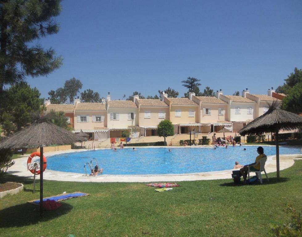 una grande piscina con persone sedute in un prato di Islantilla Casa Adosada 700 metros de la playa a Islantilla