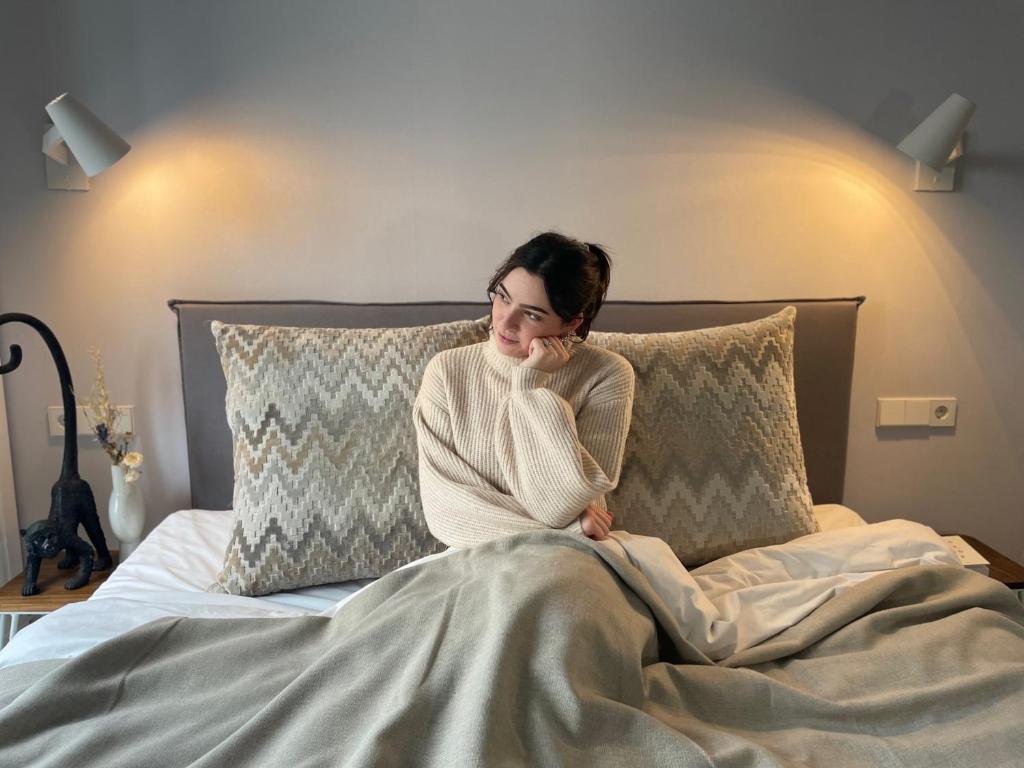 une femme assise sur un lit sous une couverture dans l'établissement Stadsvilla Hotel Mozaic Den Haag, à La Haye