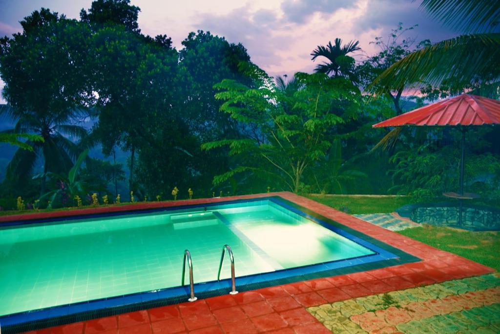 una piscina con sombrilla y árboles en Discovery resort, en Ratnapura