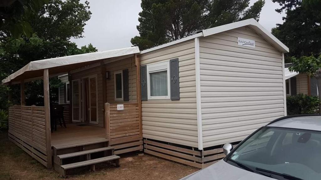 une petite maison avec une véranda et une voiture dans l'établissement MOBILHOME CAMPING 4 étoiles NARBONNE-PLAGE, à Narbonne