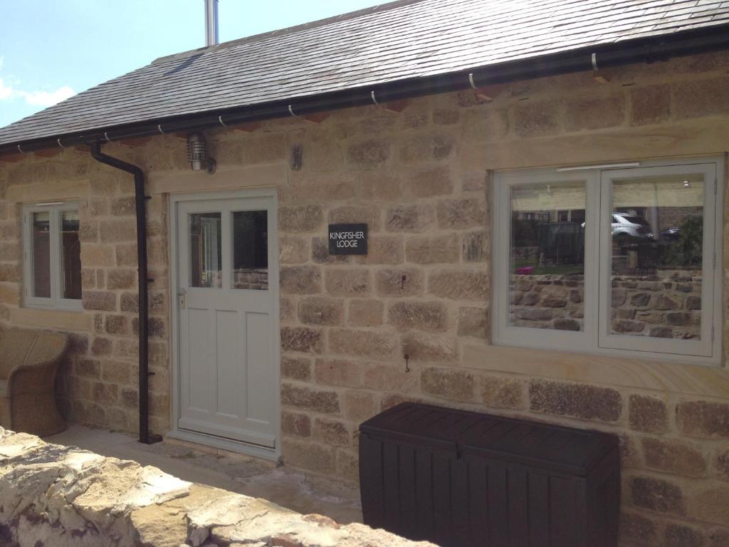 a stone building with a white door and two windows at Kingfisher Lodge in Froggatt