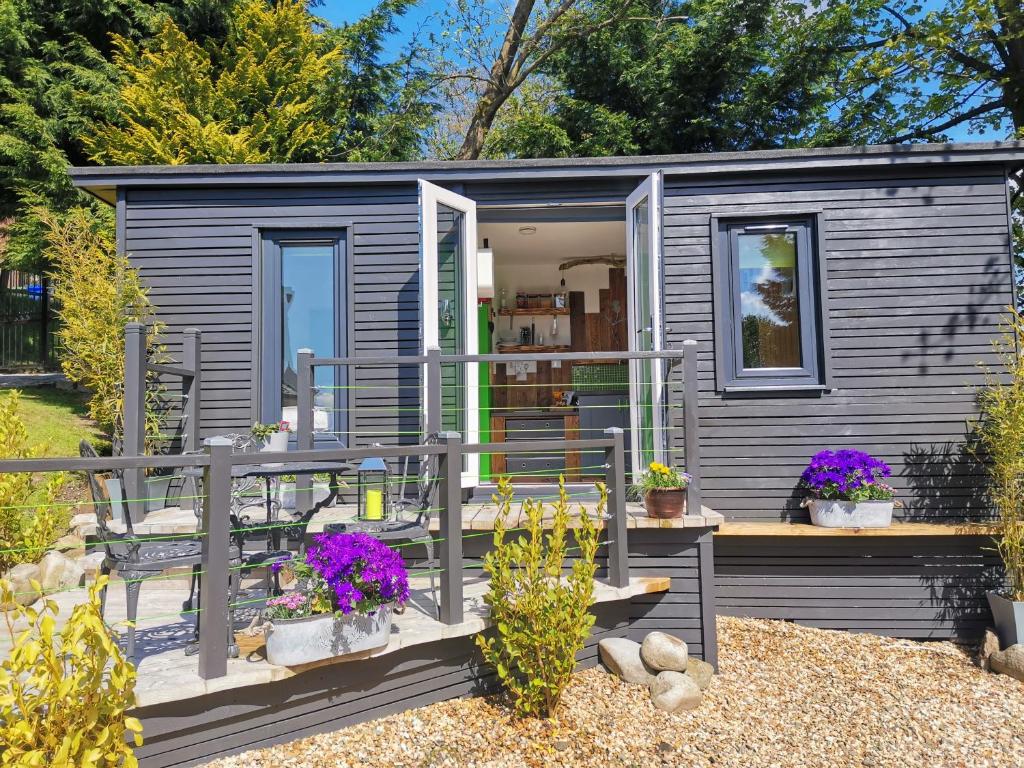 a gray tiny house with a porch and flowers at The Wee Den in Balfron