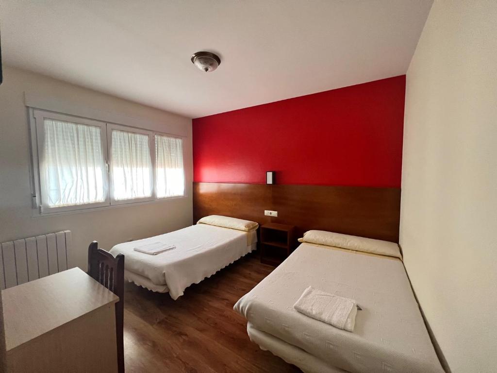 a room with two beds and a red wall at Pensión Carballeira in Arzúa