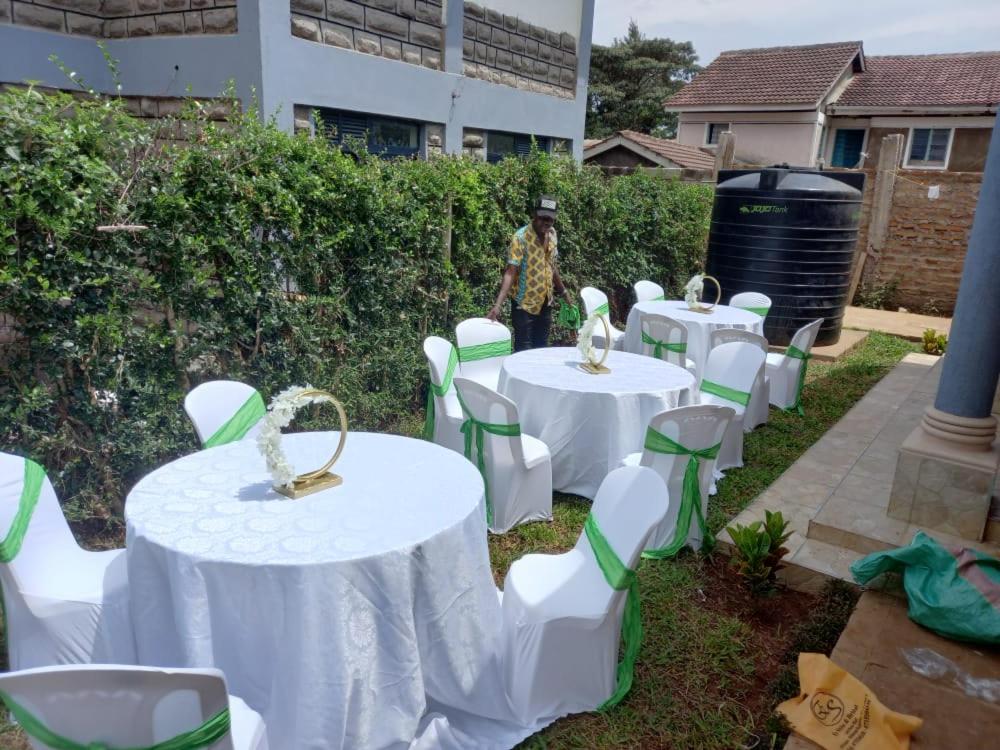 Eine Gruppe von Tischen und Stühlen mit einem Mann, der in einem Hof steht. in der Unterkunft Levans Lounge in Kisumu
