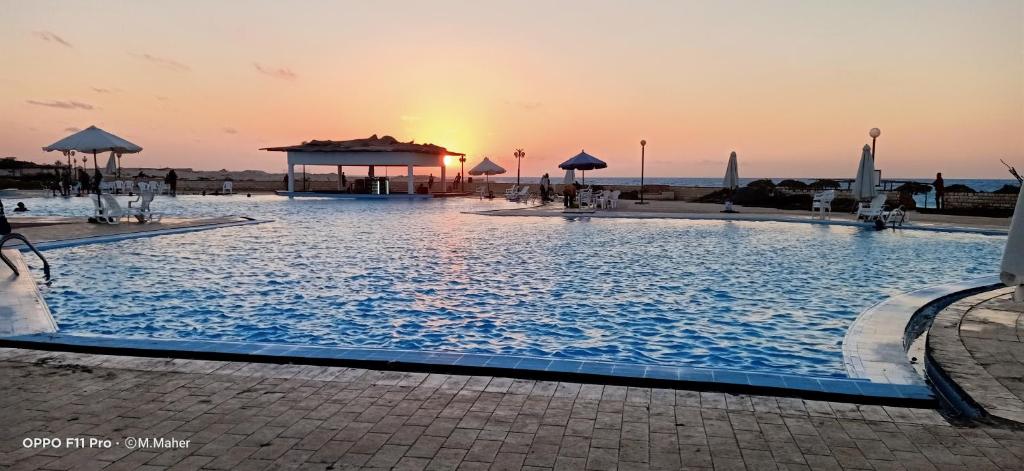 a large swimming pool with a sunset in the background at Le Beau Site Chalet in El Alamein