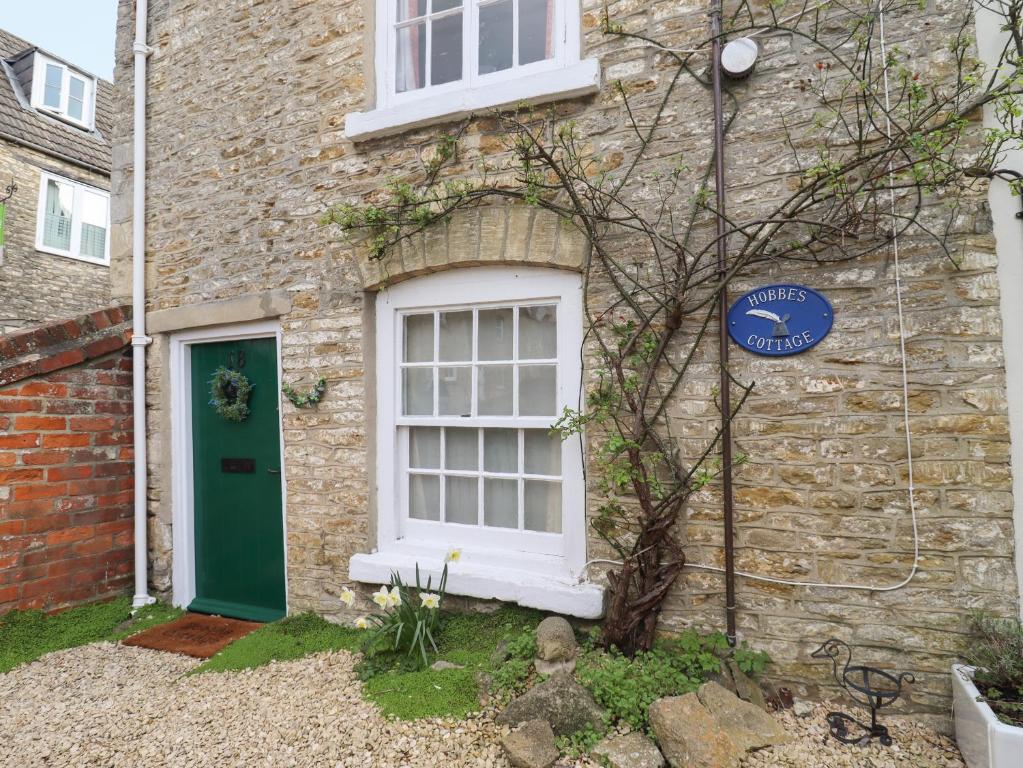 uma casa de tijolos com uma porta verde e uma janela em Hobbes Cottage em Malmesbury