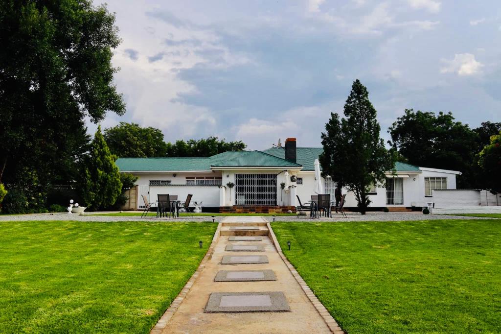 a white house with a green yard with a pathway at La Capucine in Kroonstad