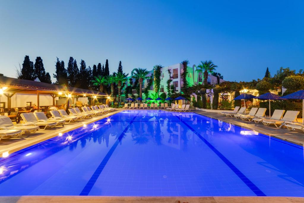 a swimming pool with chairs and umbrellas at night at Natur Garden Hotel in Bitez