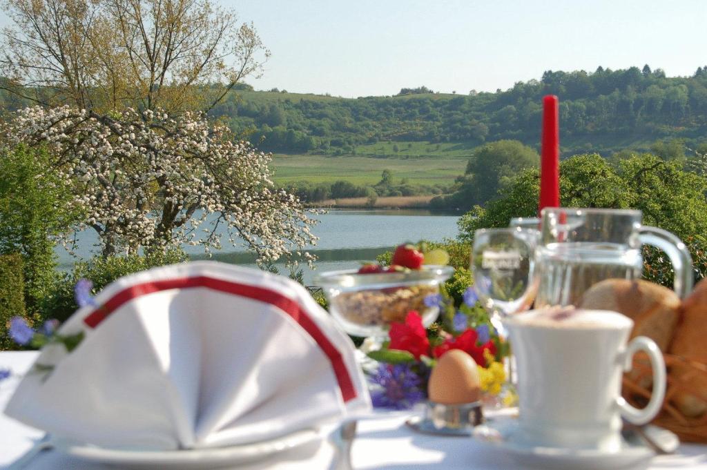 a table with food and drinks and a view of a lake at Hotel-Pension Maarblick in Schalkenmehren