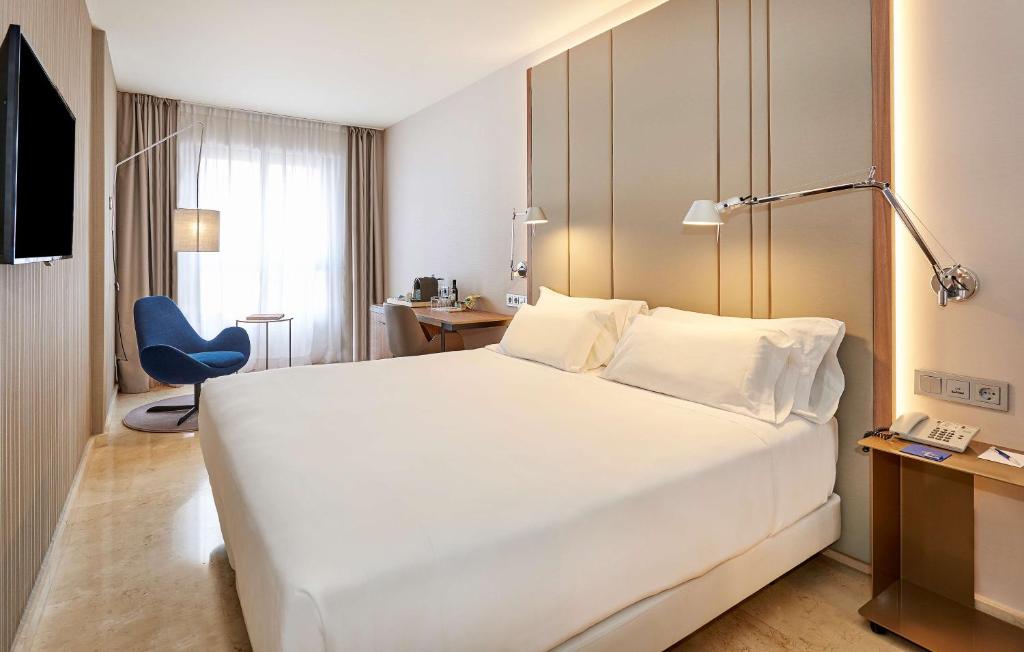 una habitación de hotel con una gran cama blanca y una silla azul en NH Logroño Herencia Rioja, en Logroño